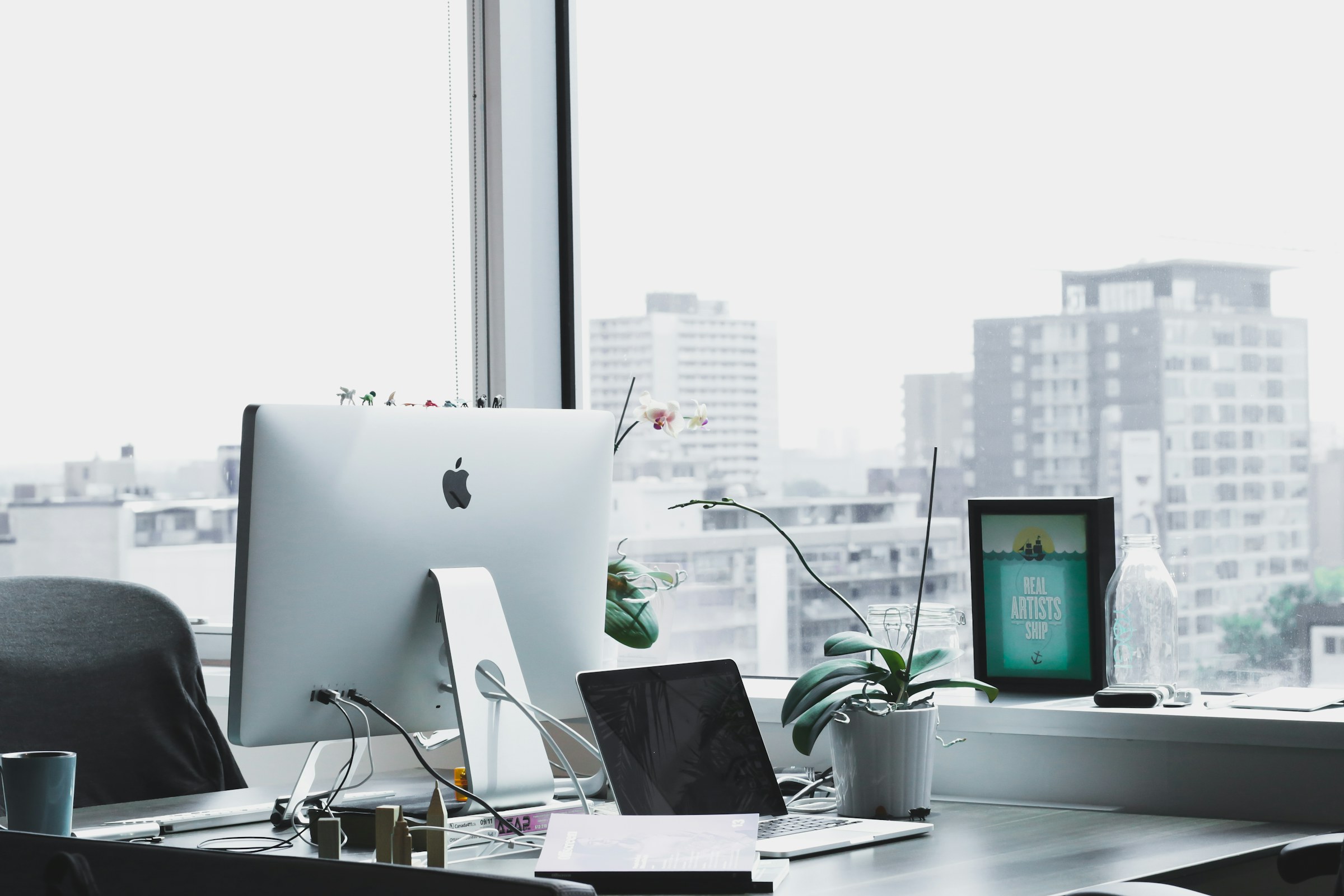 A bright workspace with a computer and laptop beside a window